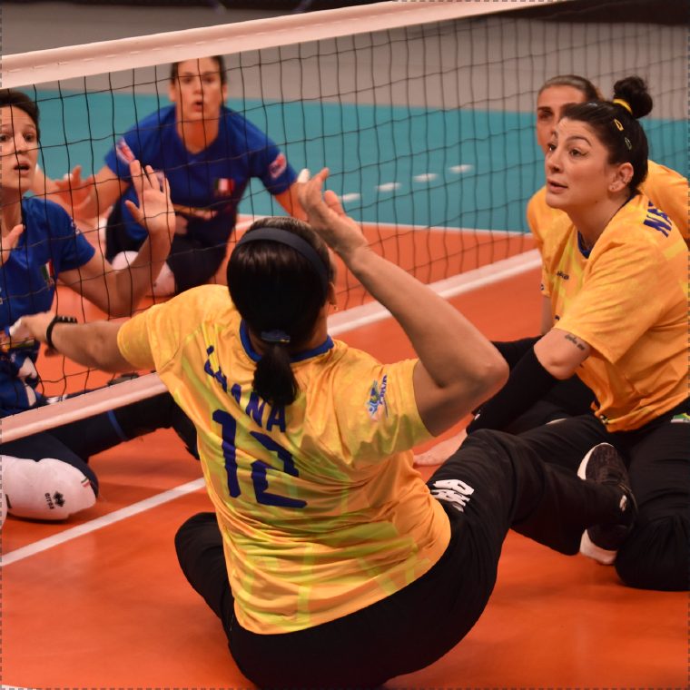 Athletes competing in sitting volleyball at the net.